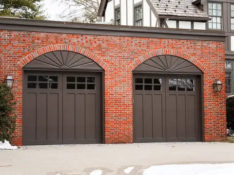 Brown carriage-house style garage doors with a row of small windows across the top, set under brick arches on a red brick Tudor house
