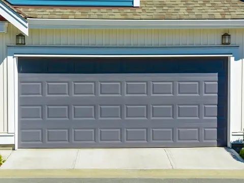 A gray raised-panel garage door, two cars wide, framed in white trim on a house with cream board-and-batten siding