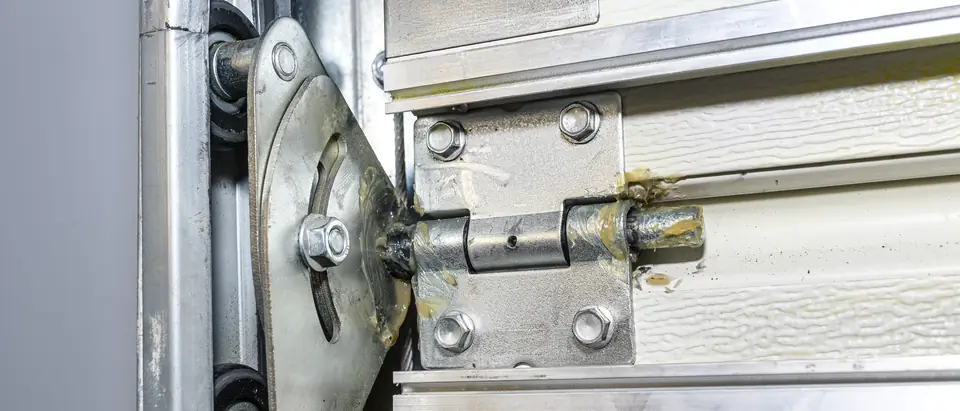 A greased hinge and roller bracket at the edge of a garage door section, with the rollers sitting in the steel track